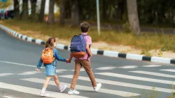 Chlapec a dievča so školskými batohmi sa držia za ruky a prechádzajú po priechode pre chodcov