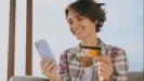 Usmiata žena vonku drží v ruke mobil a platobnú kartu