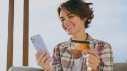Usmiata mladá žena vonku drží mobil a platobnú kartu