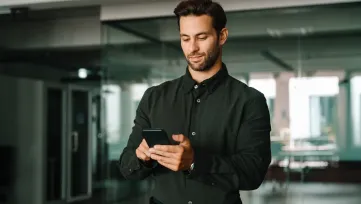Muž v košeli píše na mobile v presklenej kancelárii